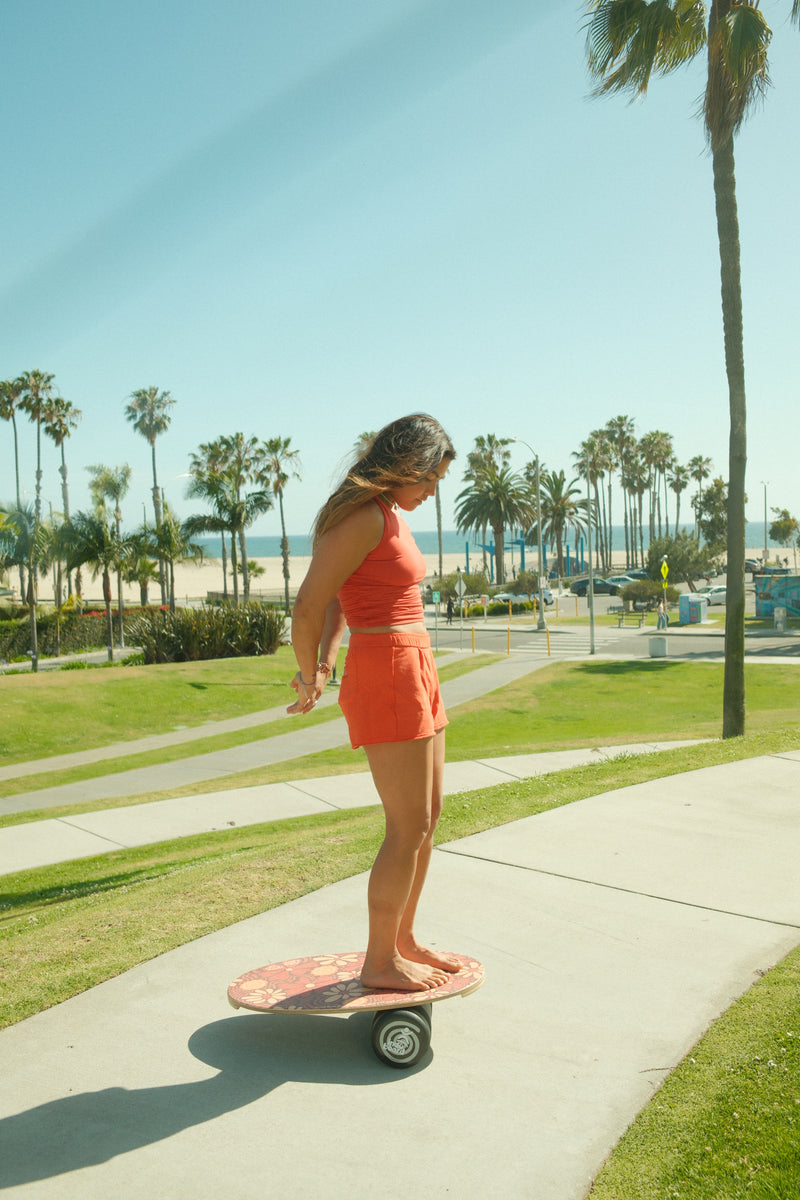 Woman trains barefoot on Indo Board balance board in park near beach, demonstrating stability practice and ergonomic board design.