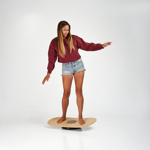 Woman on the Indo balance board featuring the Rocker model and flow cushion. Natural stain graphic.