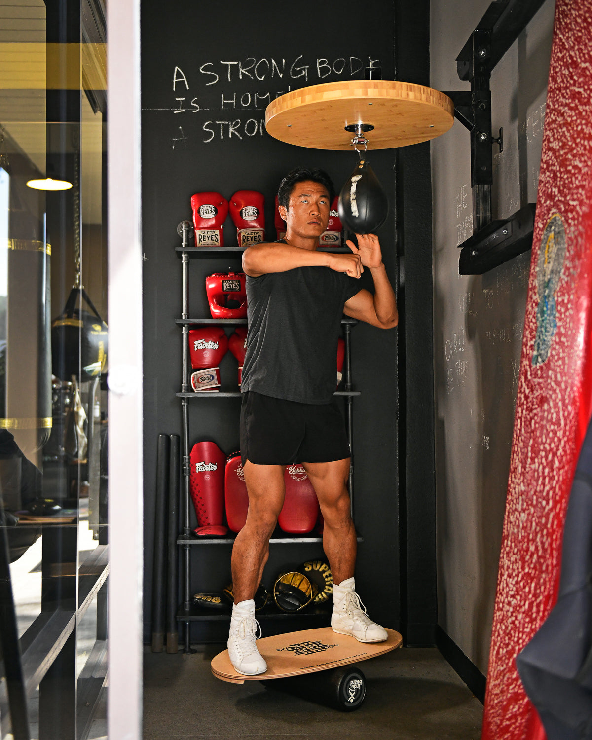 INDO BOARD Original Ola Grande with Roller Cushion in use at a gym, demonstrating balance training during speed bag workout.