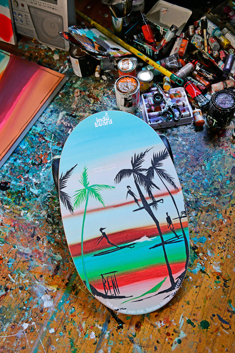 Indo Board balance board featuring a tropical beach design, showcased on a vibrant artist workspace with visible art supplies.